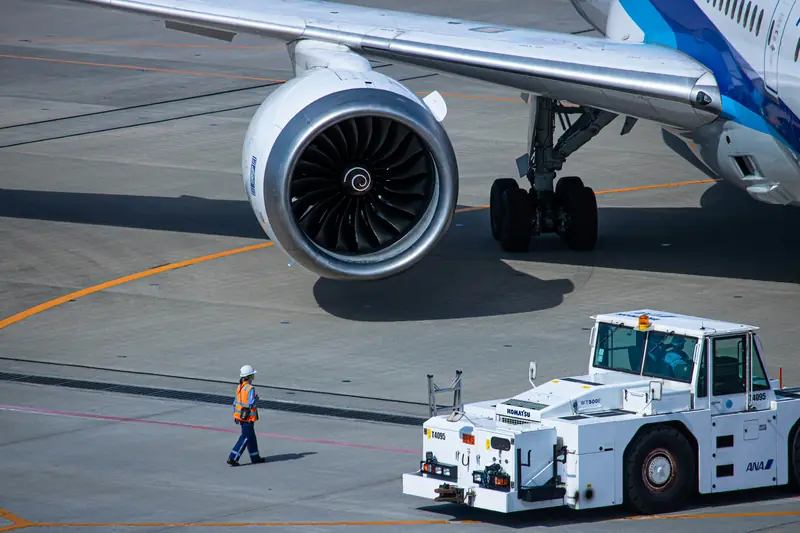 Aircraft tug and ground crew beside a jet engine on the apron